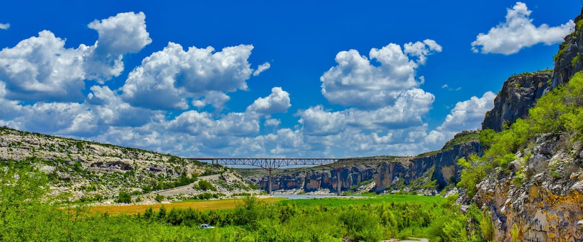 A bridge over a valley with green fields and rocky cliffs.