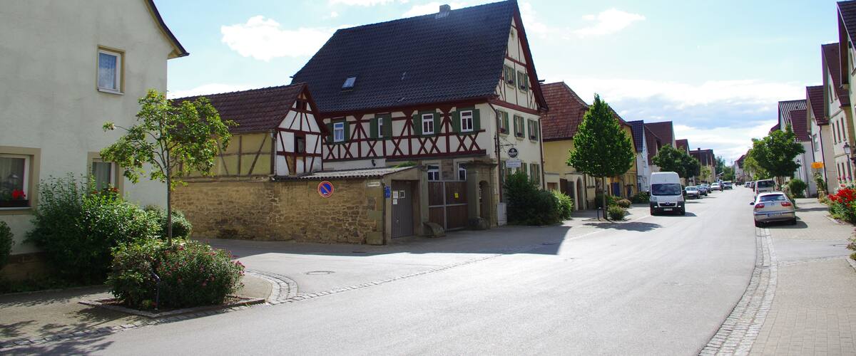 A quaint European street lined with traditional half-timbered houses, a cobblestone road, and a clear blue sky.