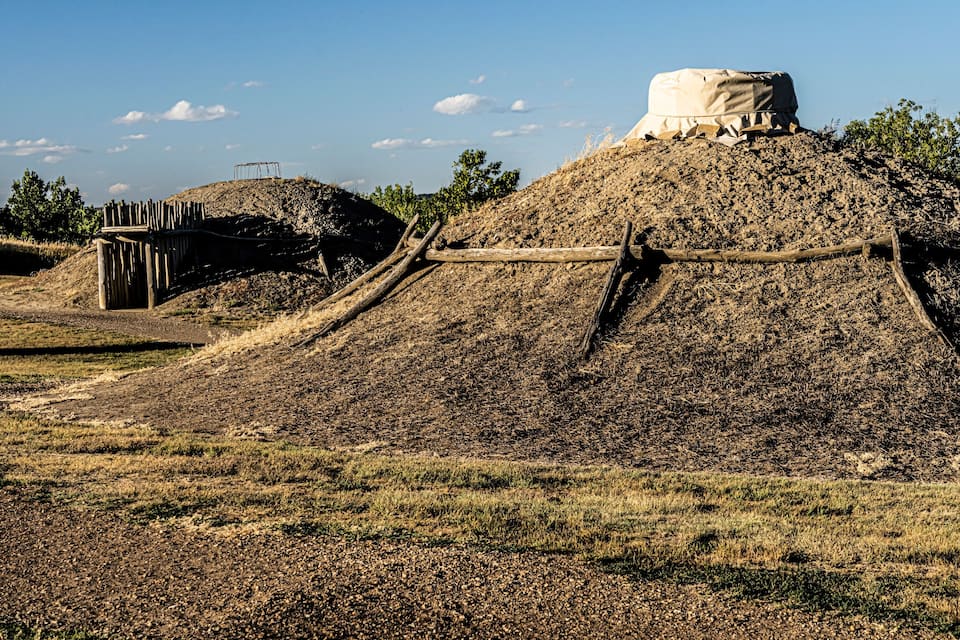 A large mound with a structure on top, surrounded by dry grassland and trees.