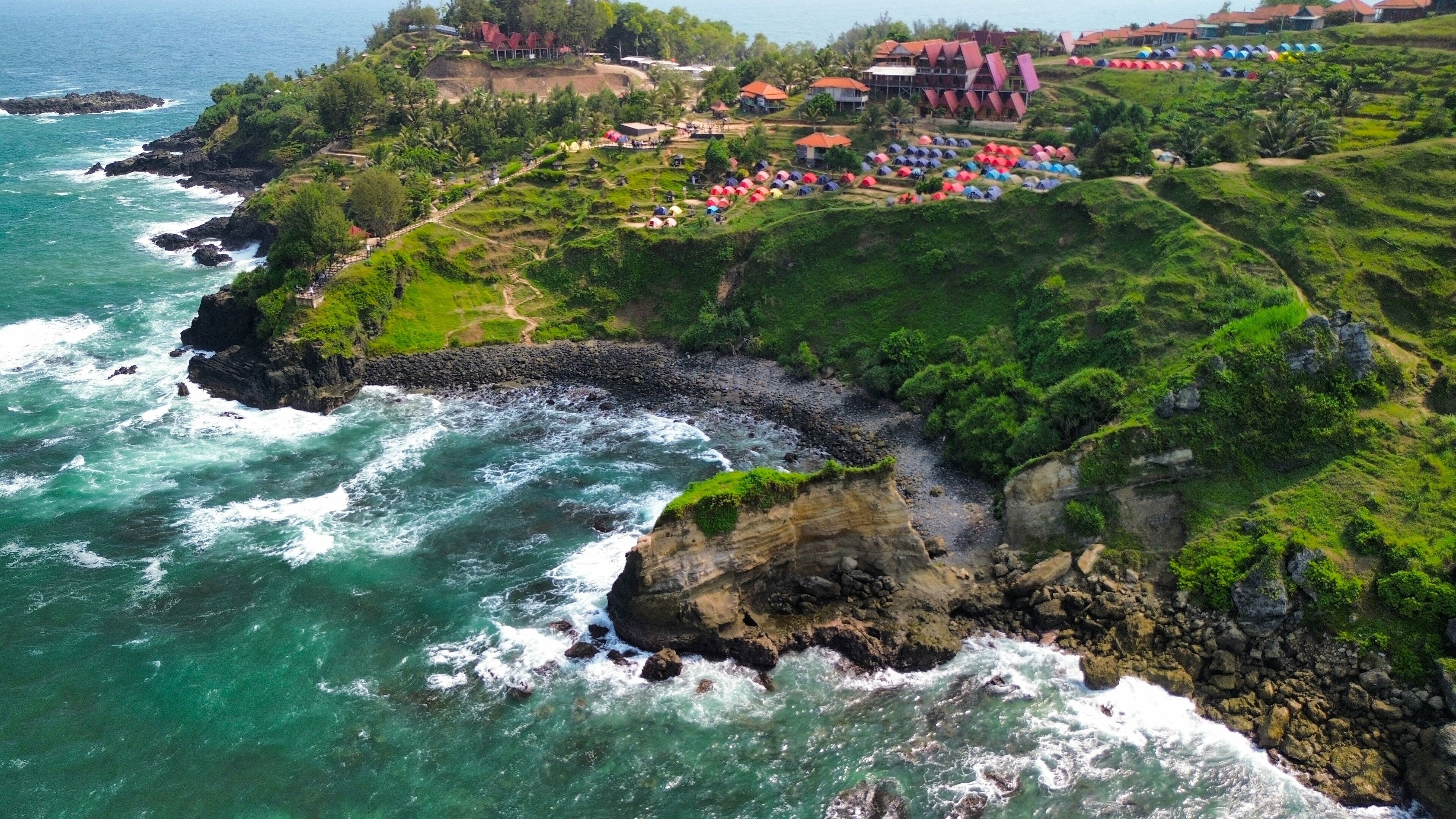 Aerial drone view of coastline with hills and trees, as well as view of coral cliffs and sea with waves from the ocean in Menganti Beach Kebumen Central Java Indonesia