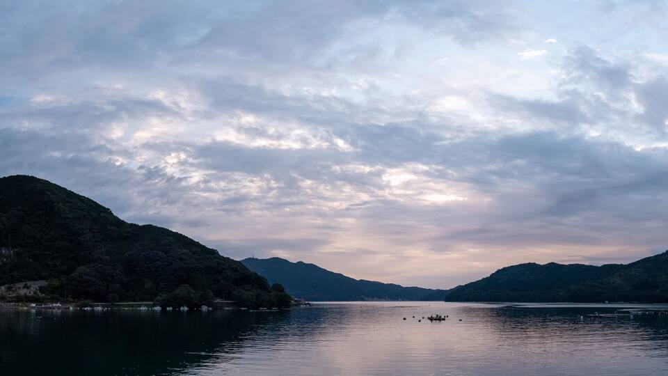 A calm lake surrounded by mountains under a cloudy sky.