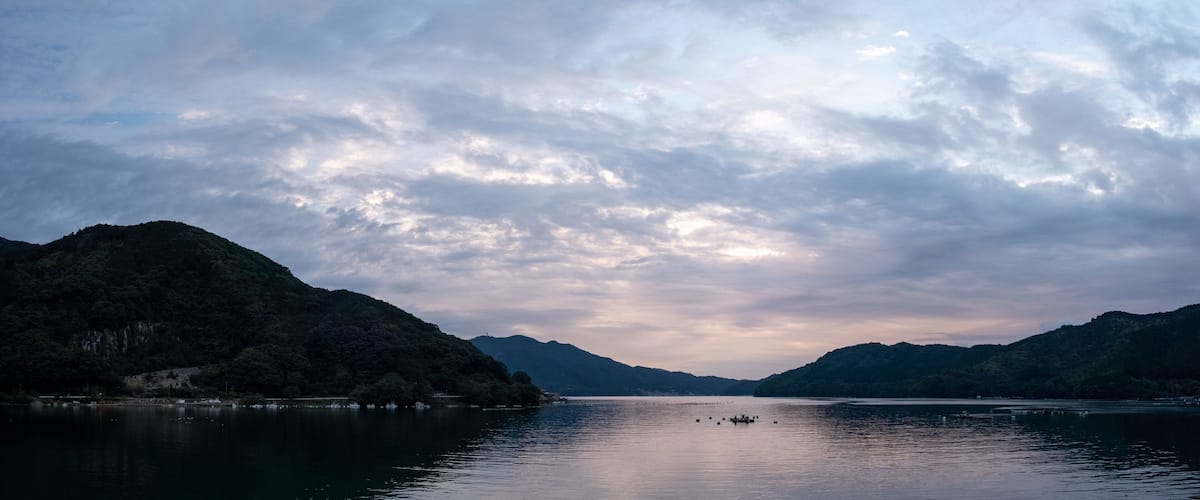 A calm lake surrounded by mountains under a cloudy sky.
