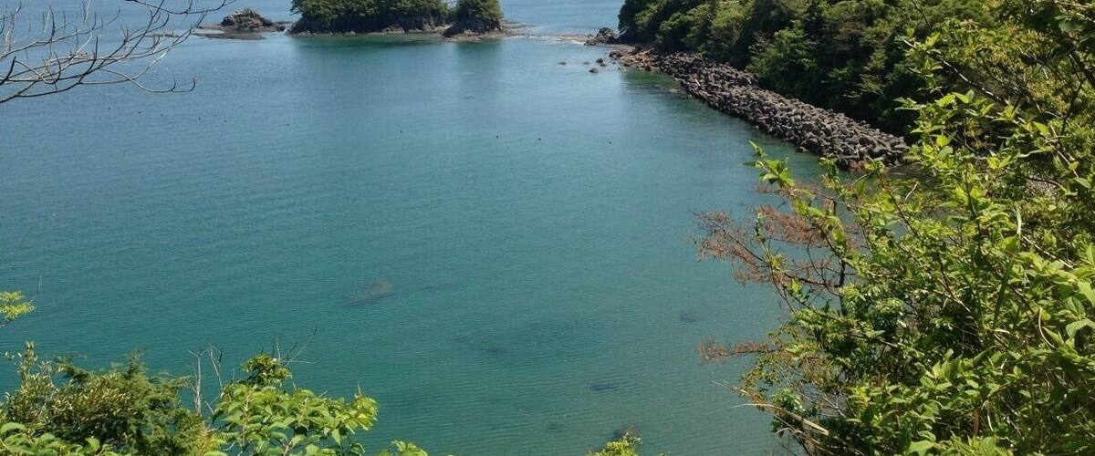 A coastal landscape with clear turquoise waters, rocky shorelines, and lush green hills.
