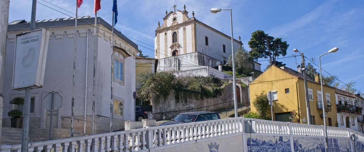 A street with a white fence, a church, and flags.