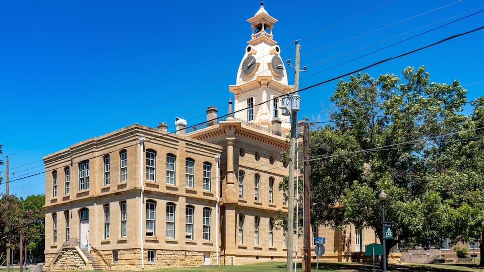 A historic building with a clock tower, large windows, and a well-maintained lawn.