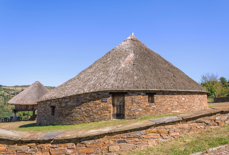 A stone building with a thatched roof, surrounded by stone walls and a grassy landscape.