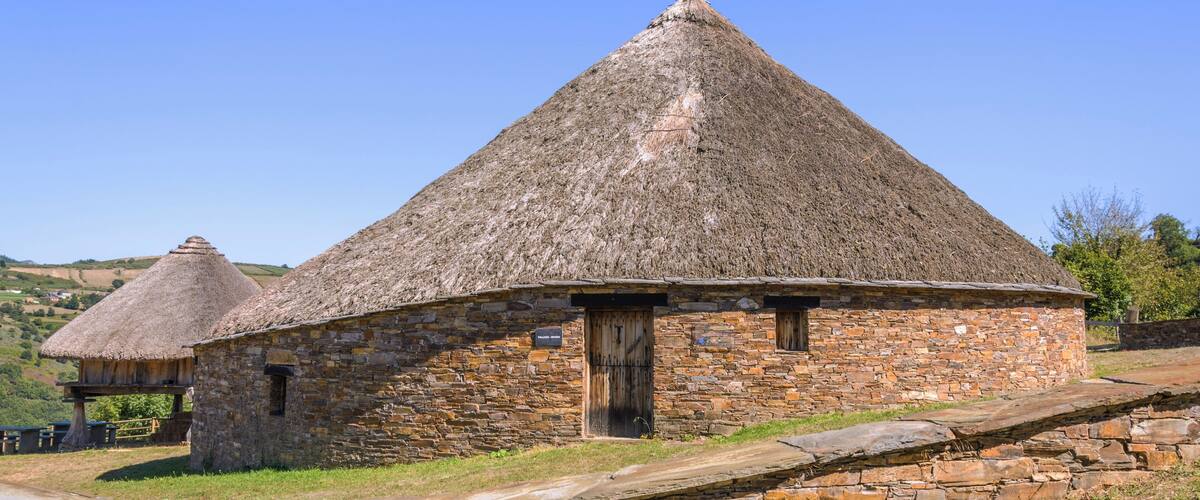 A stone building with a thatched roof, surrounded by stone walls and a grassy landscape.