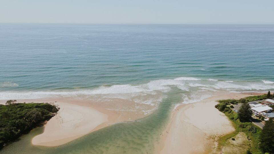 A coastal landscape with a sandy beach, clear waters, and a small settlement with houses.