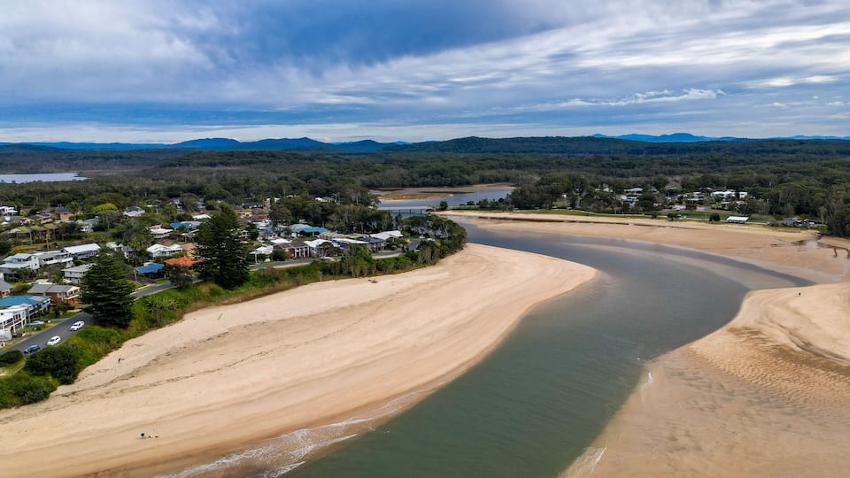 A coastal town with a sandy beach, a river, and a bridge in the distance.