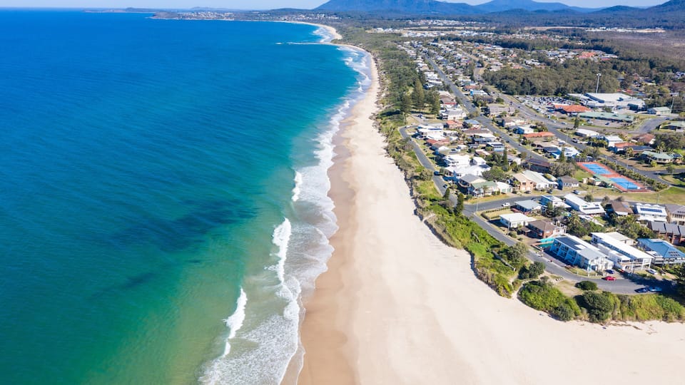 A coastal town with a beach, residential areas, and a mountain in the background.