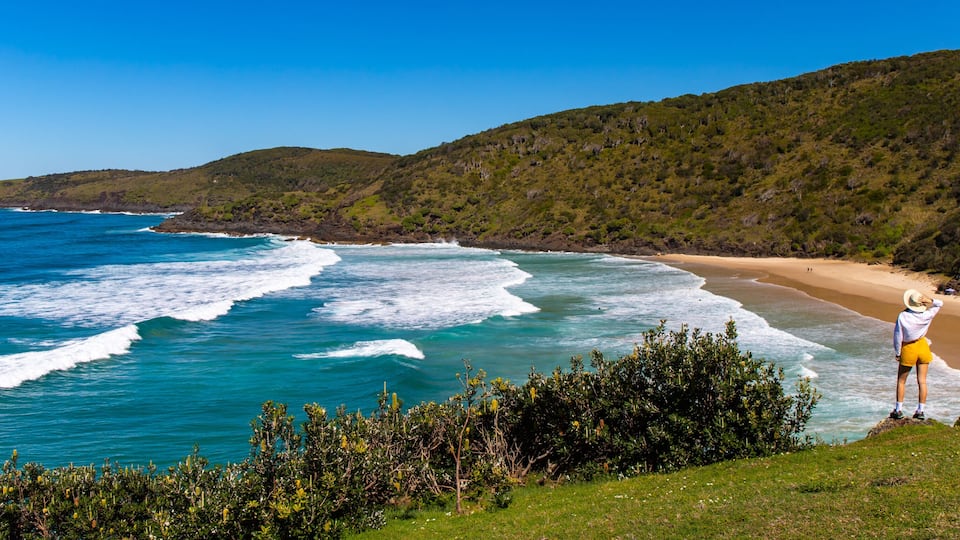 A coastal landscape with a beach, ocean waves, and green hills.