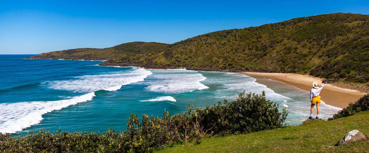 A coastal landscape with a beach, ocean waves, and green hills.