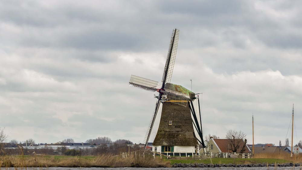View of the historic thatched Veendermolen with miller's cottage on the bosom of the Weide Aa near the Dutch village of Roelofarendsveen against the background of a winter cloudy sky