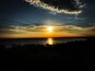 A sunset over a body of water with silhouettes of trees and a distant shoreline.