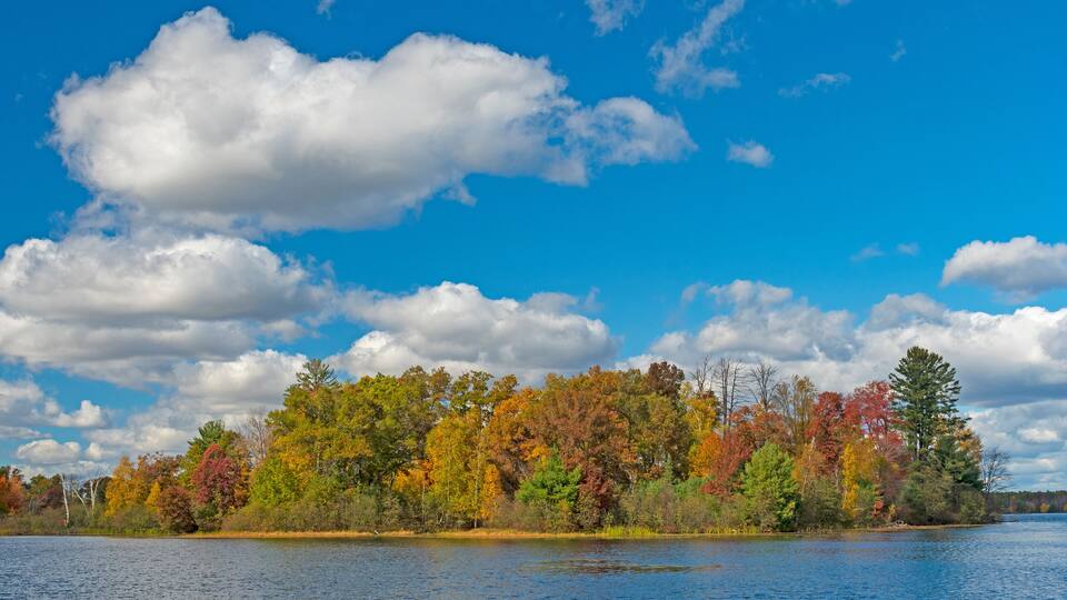 A lake surrounded by autumn-colored trees and a partly cloudy sky.