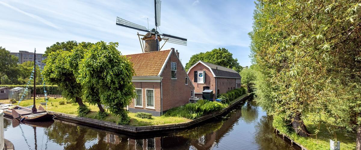 Scenic view of a traditional Dutch windmill and house by a canal on a sunny day in the Netherlands.