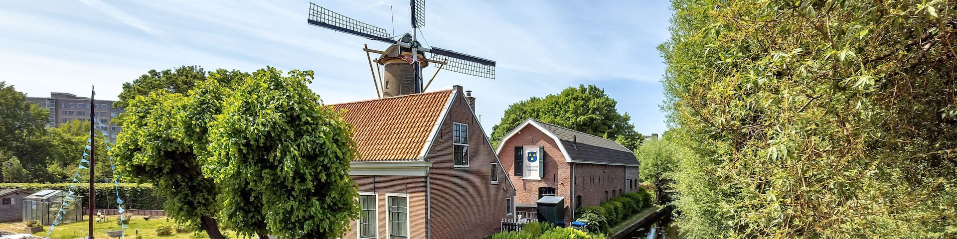 Scenic view of a traditional Dutch windmill and house by a canal on a sunny day in the Netherlands.