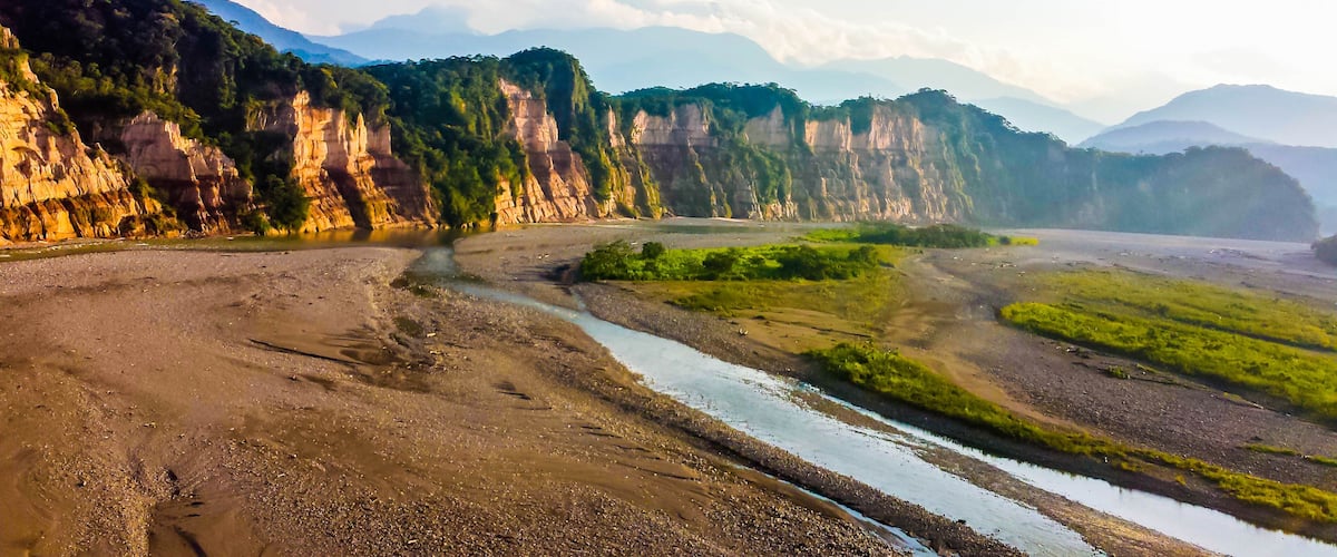 A river flowing through a valley with steep cliffs and lush greenery.