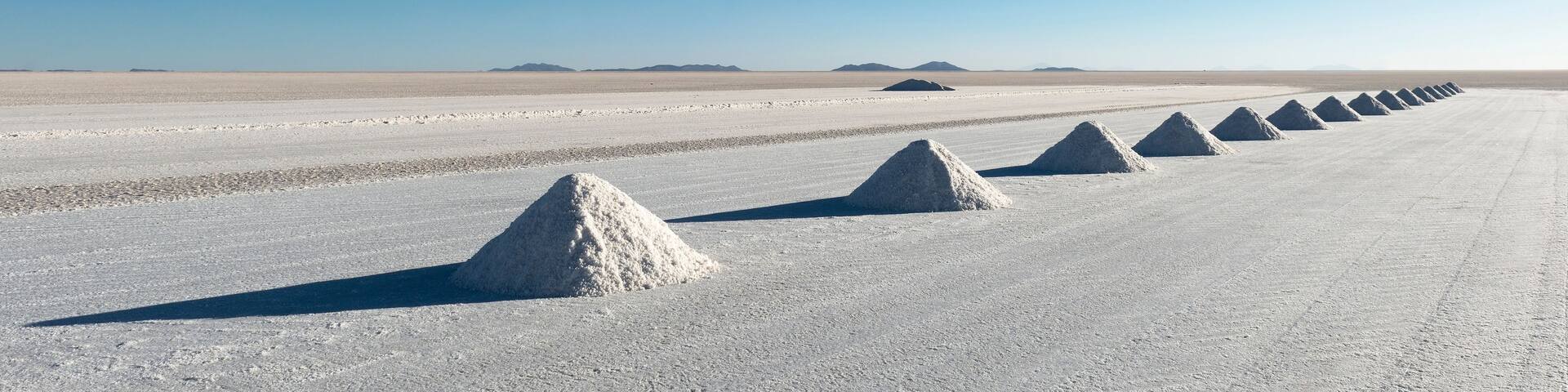 A vast salt flat with a series of conical salt piles in the foreground and distant mountains under a clear blue sky.
