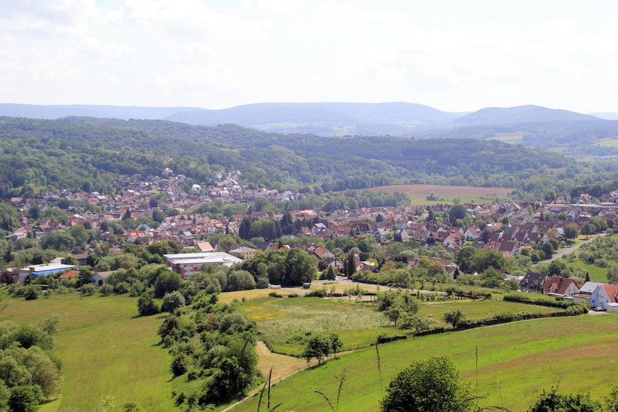 Un paysage rural avec un village, des champs verdoyants et des collines douces en arrière-plan.