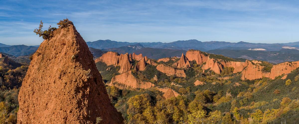 A rugged landscape with prominent red rock formations and a dense forested valley.