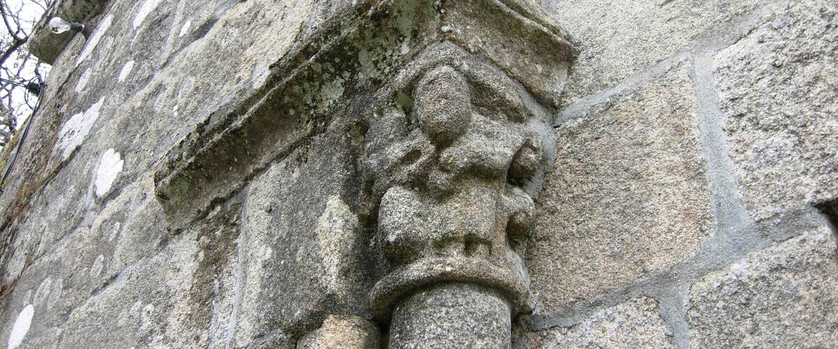 A stone building with a carved column and a triangular pediment.