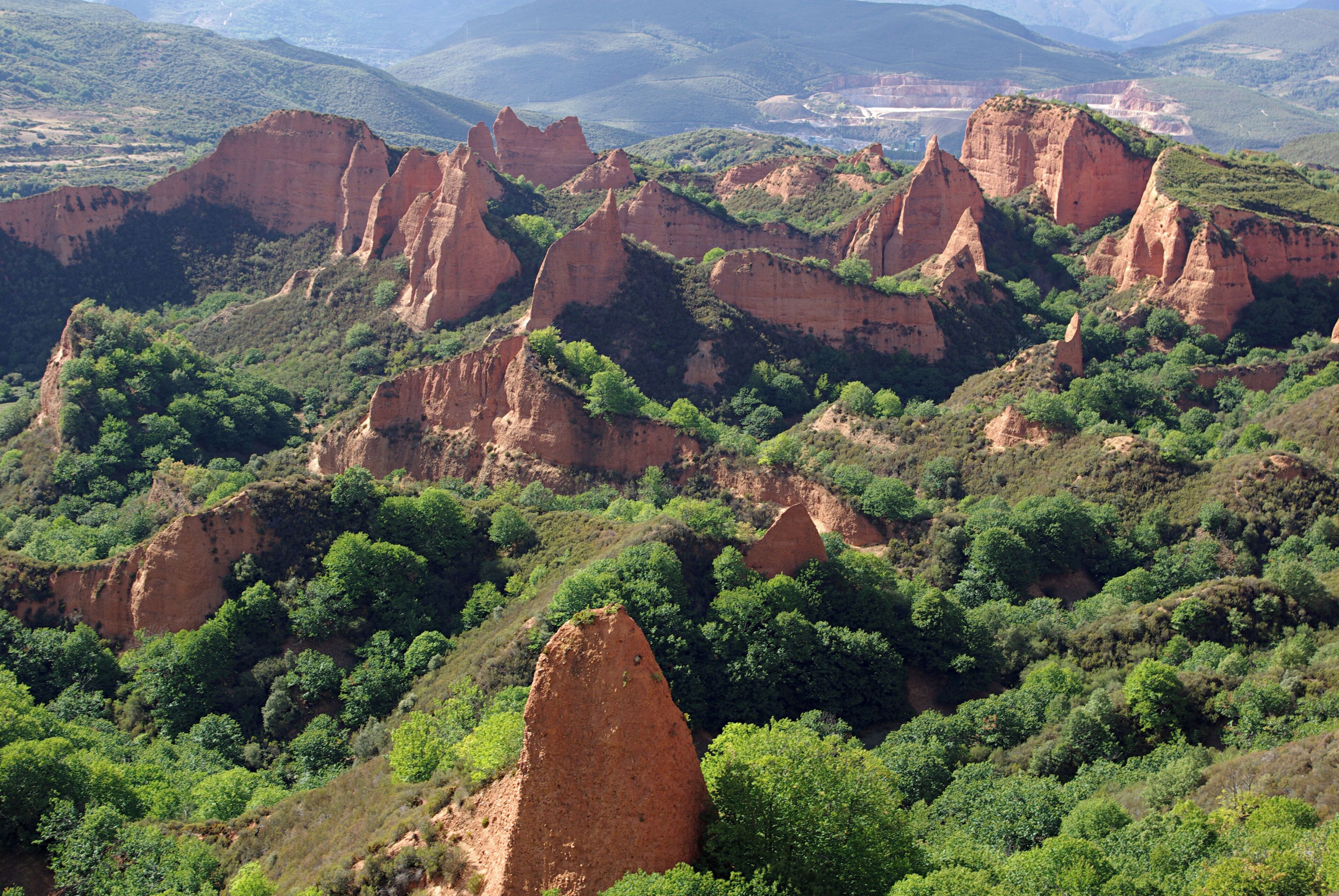 A rugged landscape with prominent red rock formations and dense green vegetation.