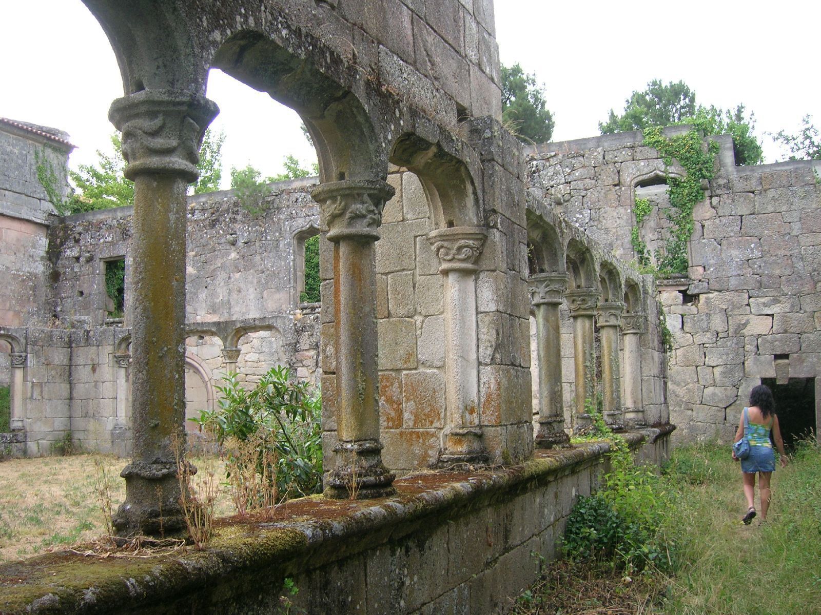 An ancient stone structure with columns and arches, overgrown with vegetation.