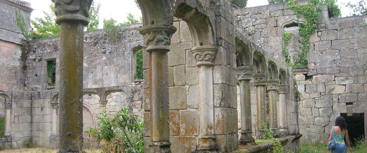 An ancient stone structure with columns and arches, overgrown with vegetation.