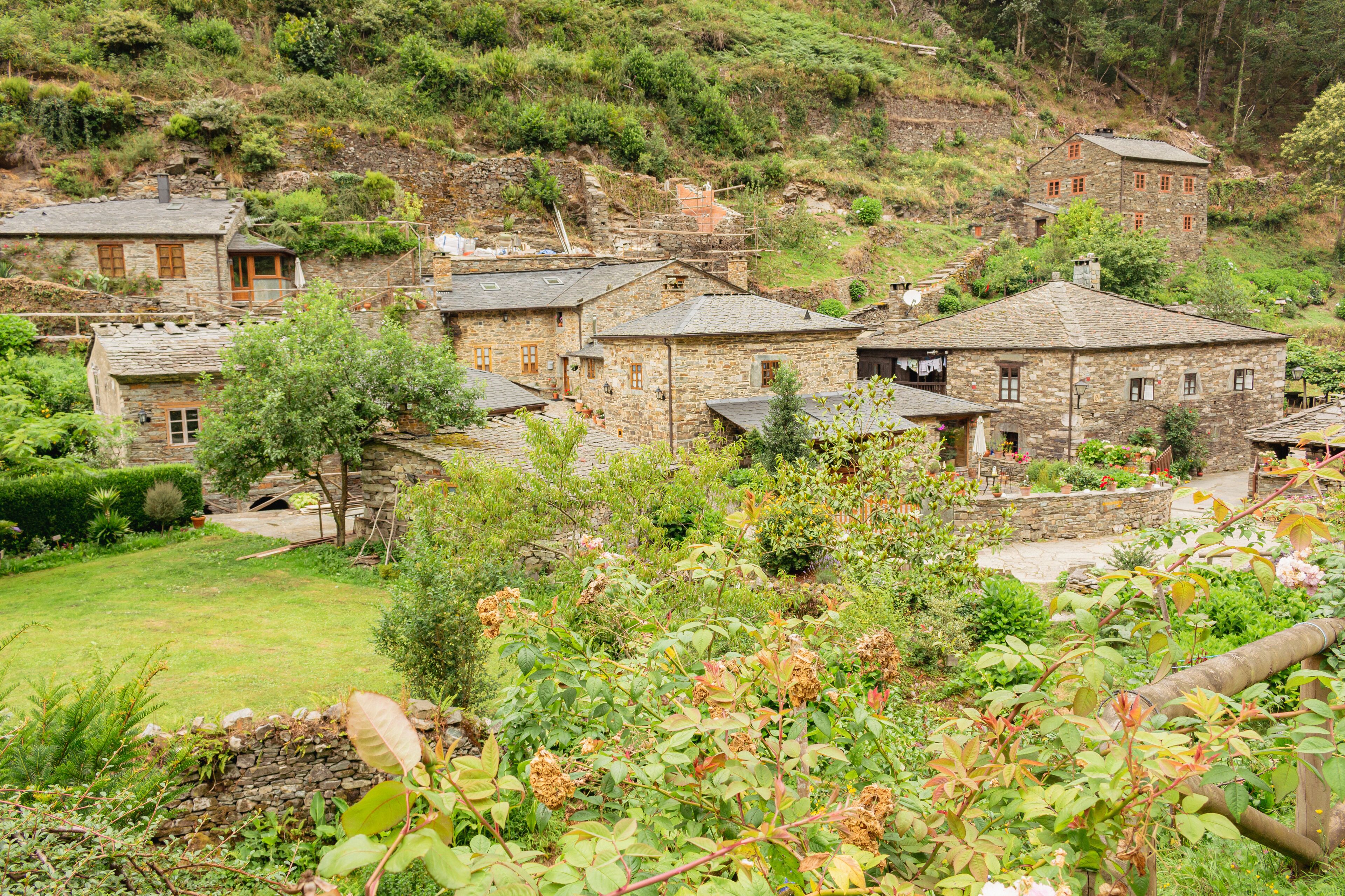 A stone village with traditional houses surrounded by lush greenery and hills.