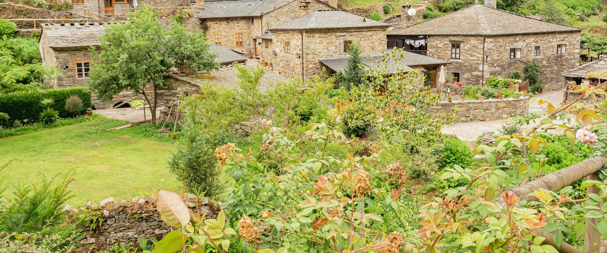 A stone village with traditional houses surrounded by lush greenery and hills.