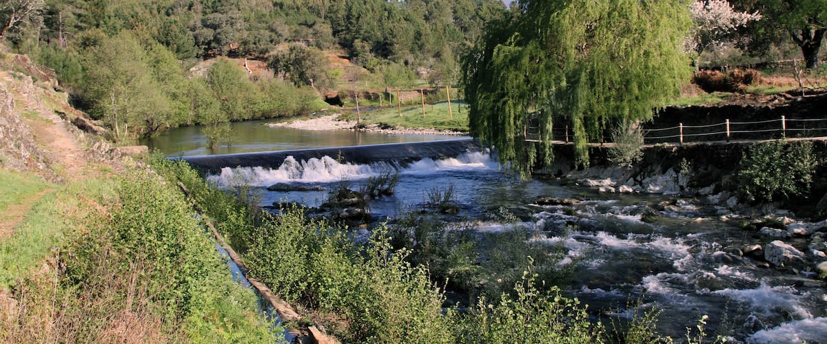 A river flowing through a valley with a small dam and a wooden bridge.