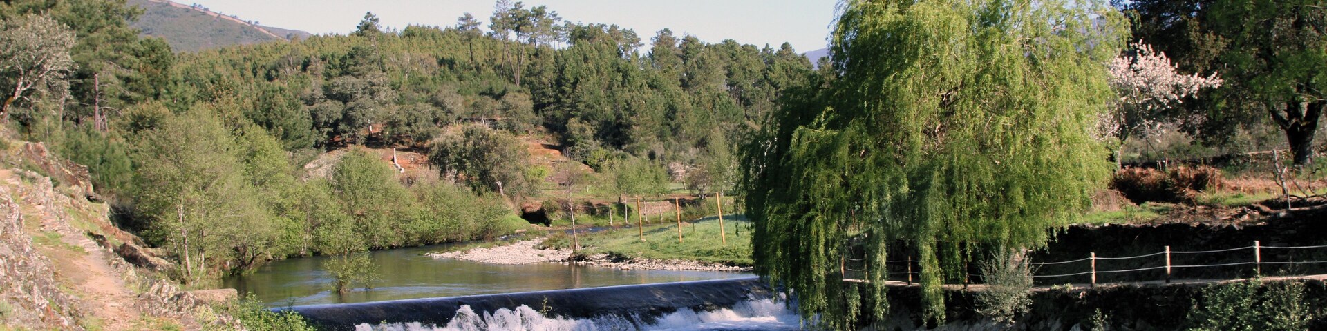 A river flowing through a valley with a small dam and a wooden bridge.
