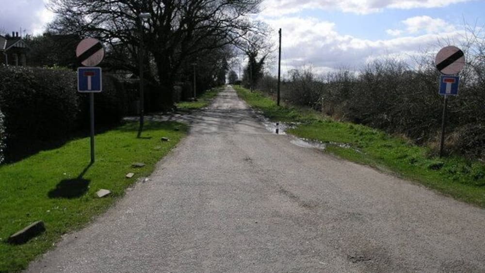 Une route de campagne avec un panneau indiquant la vitesse maximale autorisée, un panneau d’interdiction d’accès et un panneau de direction.