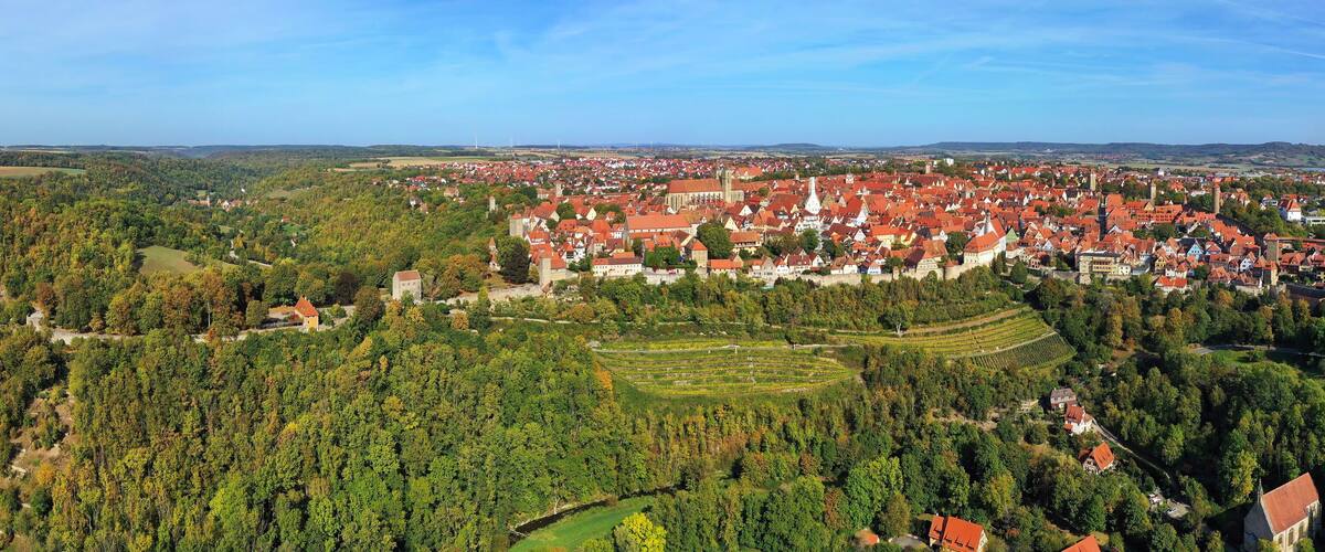 A town with red-roofed buildings surrounded by dense forests and rolling hills.