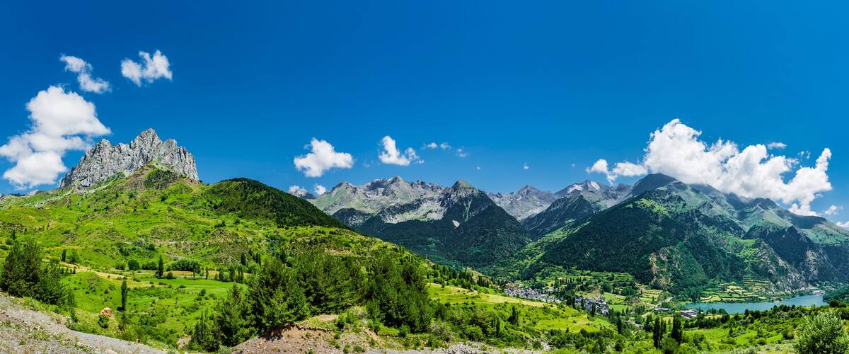 A mountainous landscape with a prominent rocky peak, lush green valleys, and a small village.