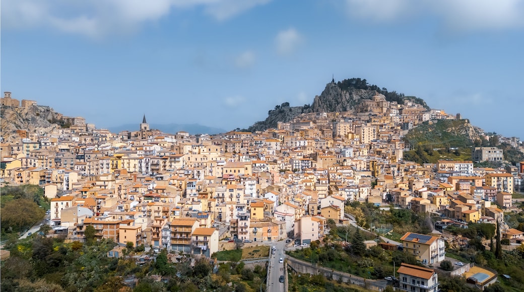 Hilltop town with rocky cliff and many buildings under tiled roofs on sunny day, Nicosia, Sicily, Italy