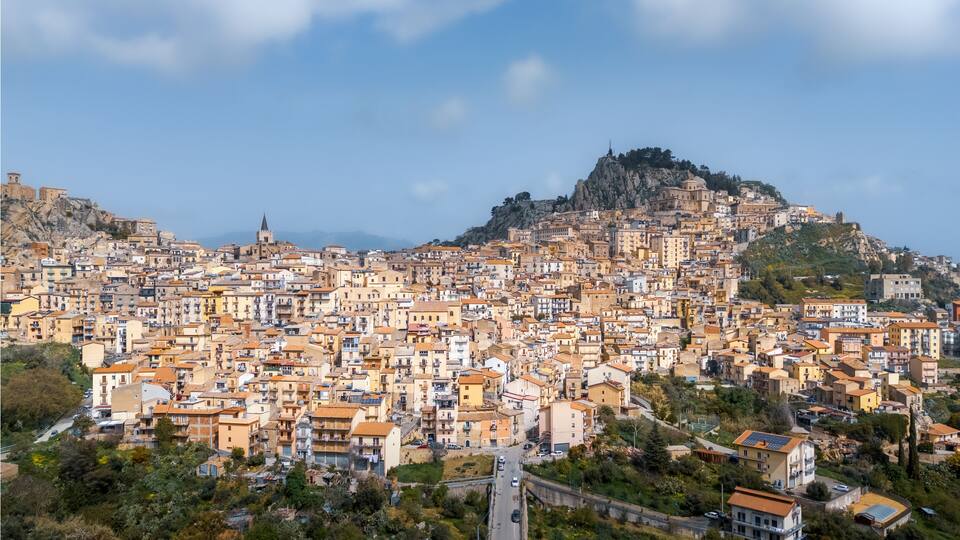 Hilltop town with rocky cliff and many buildings under tiled roofs on sunny day, Nicosia, Sicily, Italy
