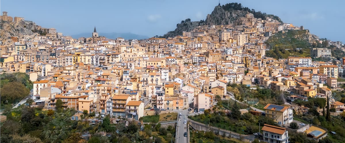 A densely packed hillside town with historic architecture, a prominent church, and a rocky hilltop.