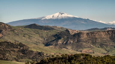 A snow-capped mountain with a clear sky, rolling hills, and scattered buildings.