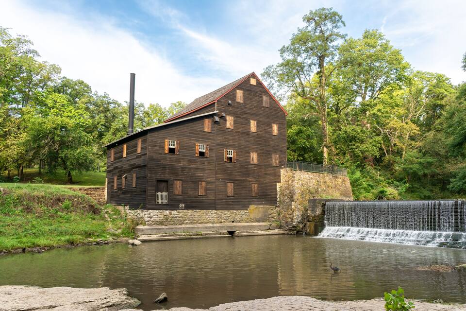 A wooden mill with a water wheel and a stone wall.