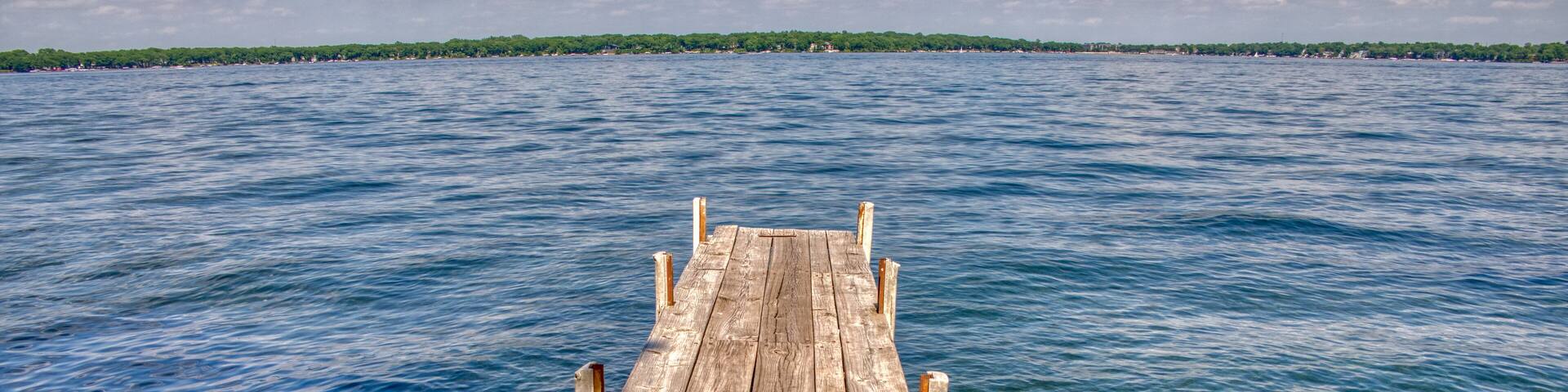 A wooden pier extending into a calm body of water with a distant shoreline and a partly cloudy sky.