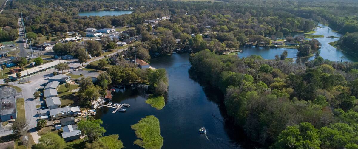 An aerial view of a river winding through a densely wooded area with a small marina and residential buildings along the banks.