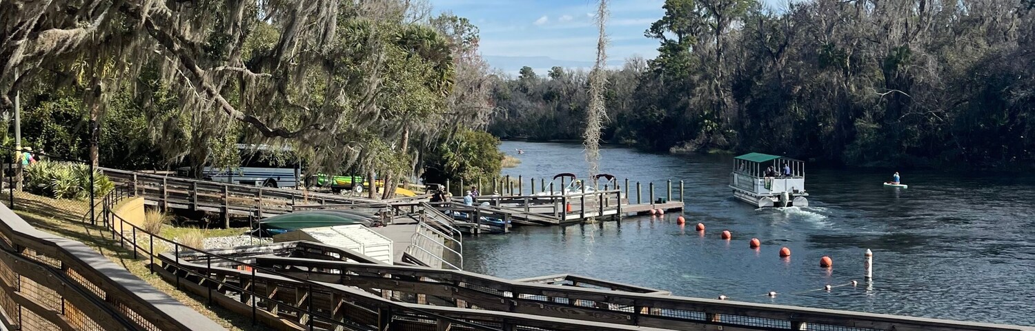 Parque a la orilla del río con bancos de madera, un muelle y un bote.