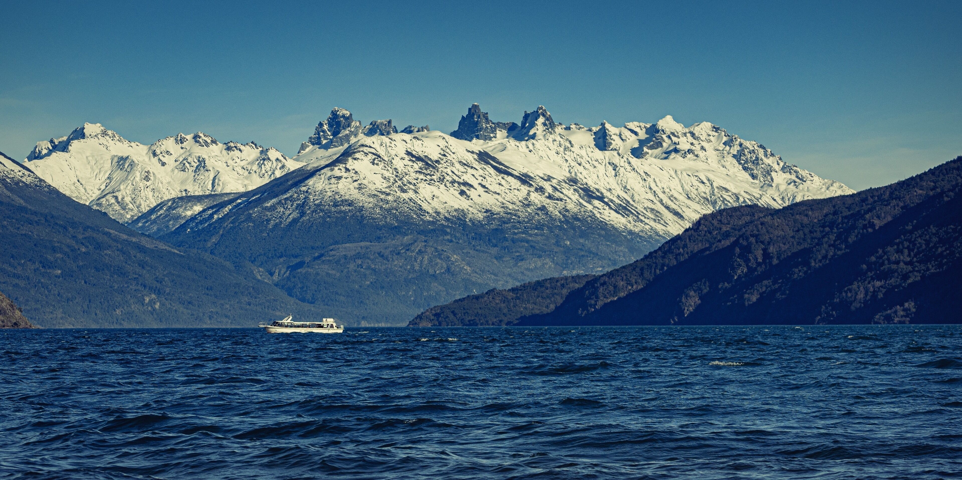 A boat on a calm sea with snow-capped mountains in the background.