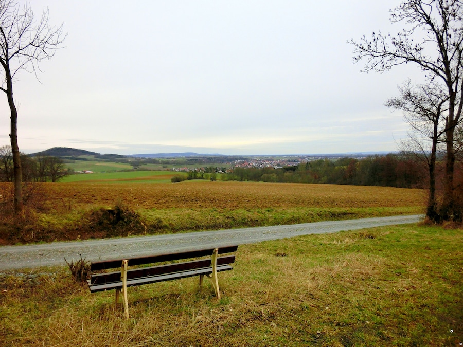 Un banco con vistas a un paisaje rural con campos, árboles y un pueblo lejano.