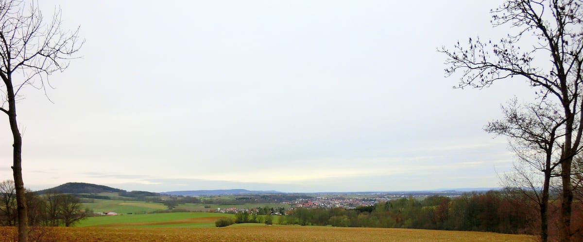A bench overlooking a rural landscape with fields, trees, and a distant town.