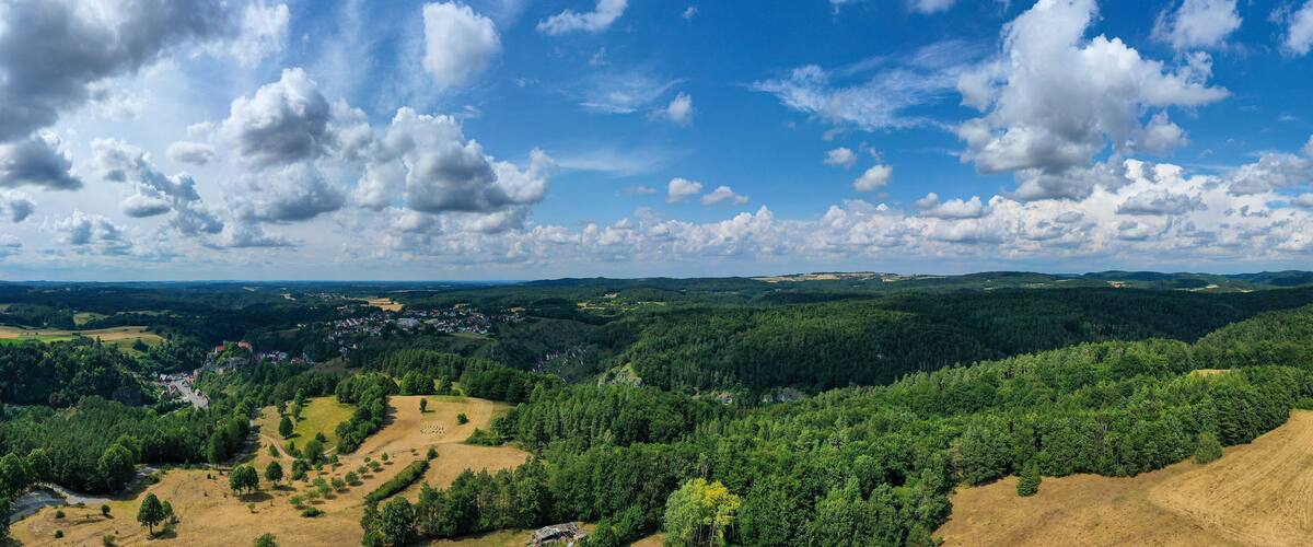 A mountainous landscape with dense forests, a small village, and a clear blue sky with scattered clouds.