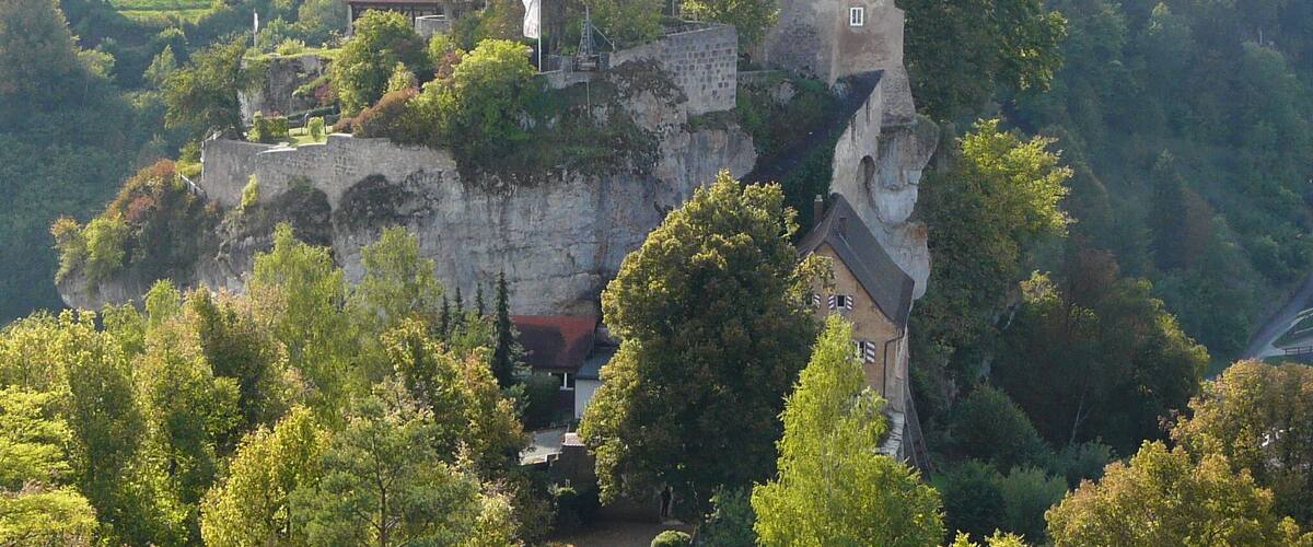 Un château perché au sommet d’une falaise, entouré d’une végétation luxuriante.
