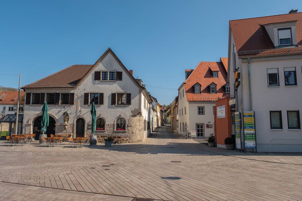 A cobblestone square with historic buildings, a fountain, and outdoor seating.